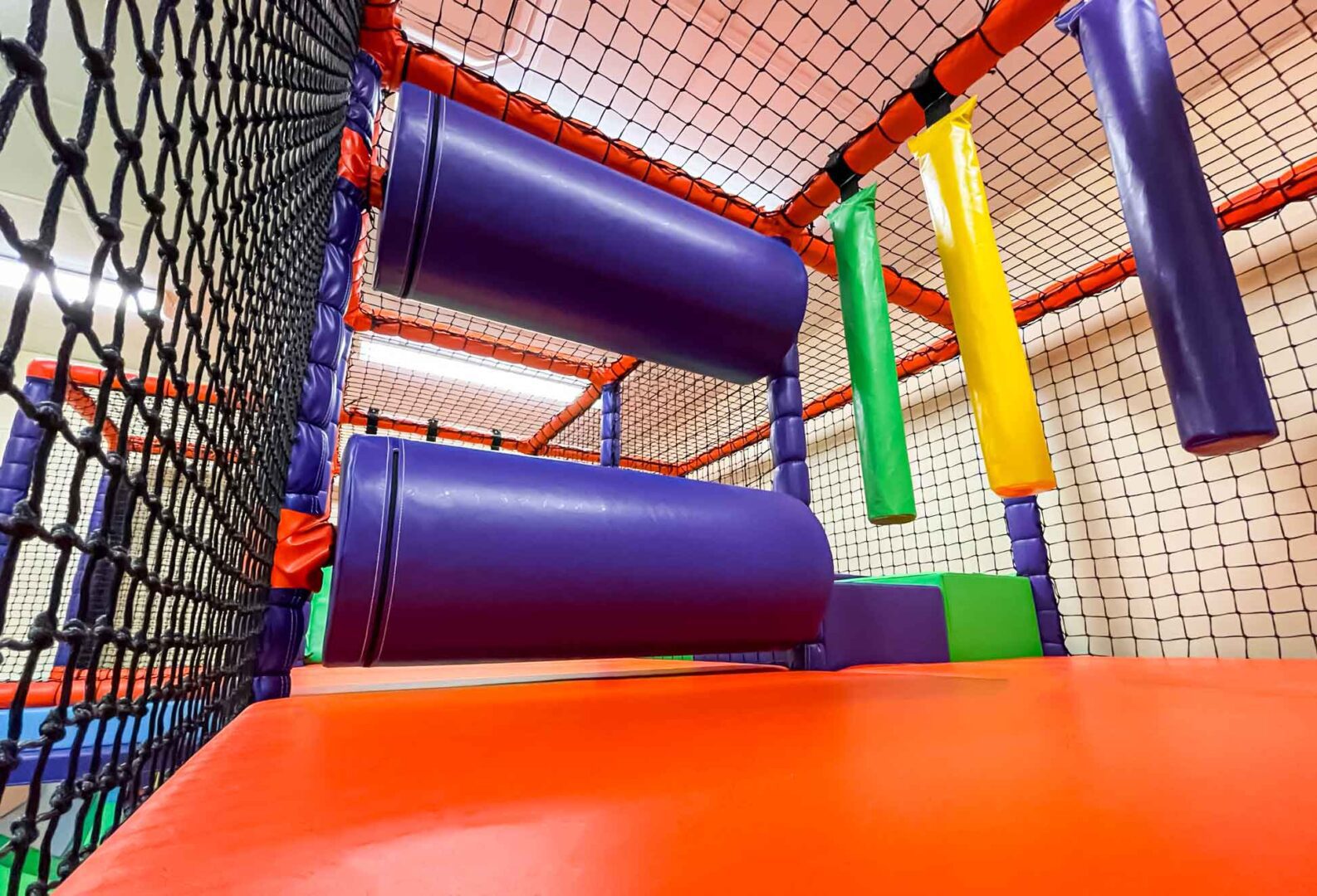 Purple and orange horizontal rollers found at St Giles school's indoor softplay area, with a yellow and a green hanging snake in the background. Designed by Play Creations.