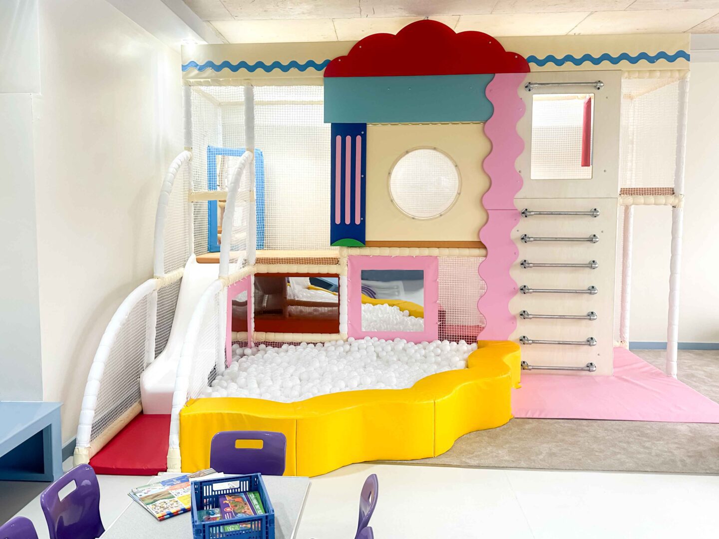 It Takes a Village indoor softplay featuring a cream, yellow and pink overall colour scheme. The softplay features a ball pit, a slide and metal ladder rungs leading inside the softplay. Designed by Play Creations