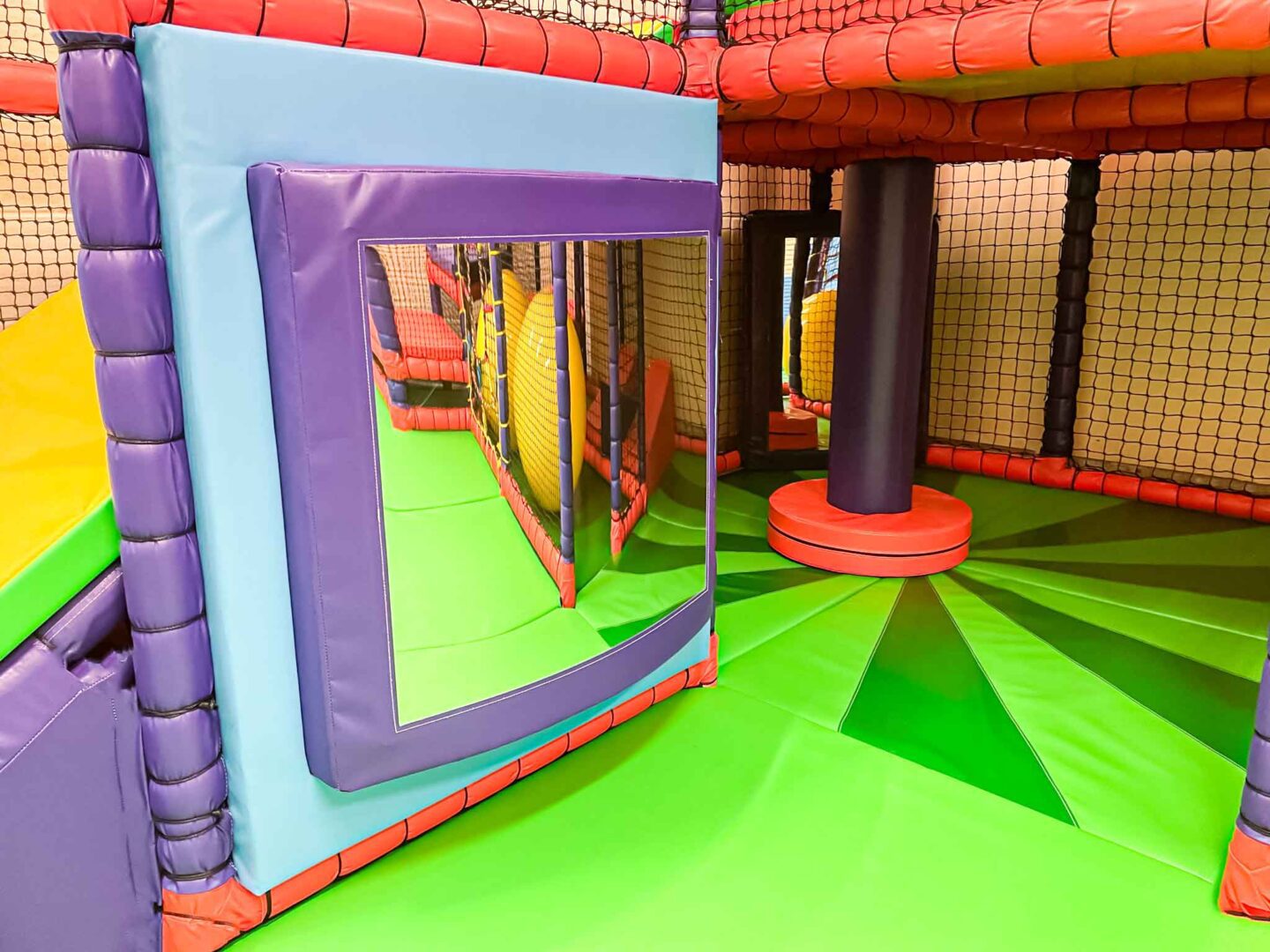 Blue and Purple Wobble Mirror and backboard at St Giles School's indoor softplay area. Designed by Play Creations to have a bright and bold scheme