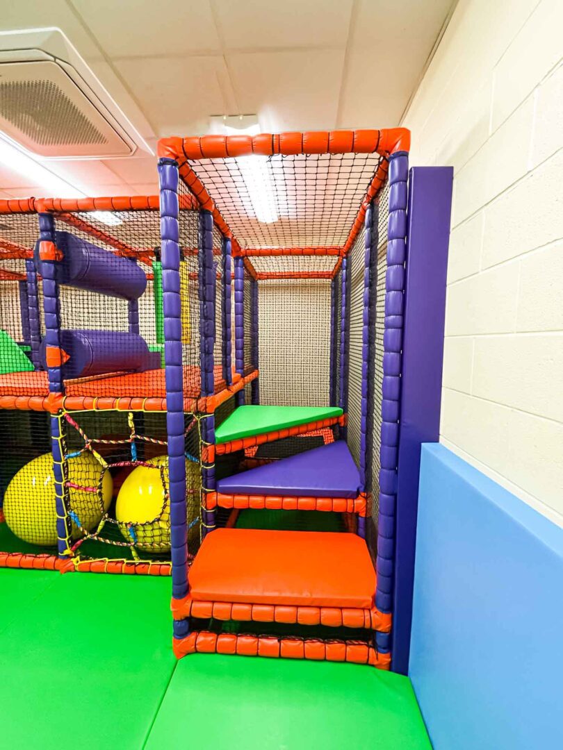 Corner Climb front view. Orange, purple and green steps leading the first floor of the softplay. Found at St Giles School.