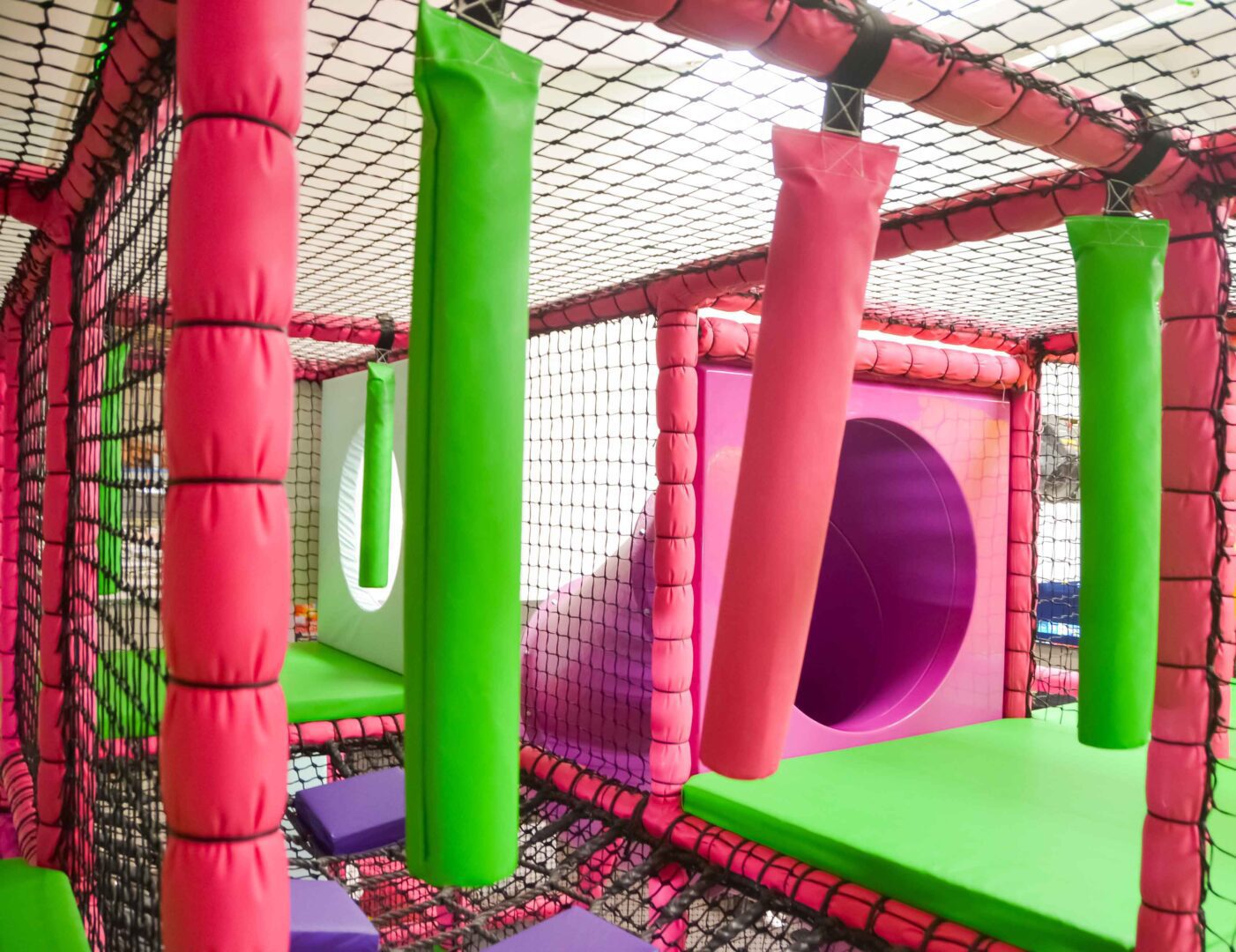 Green and Pink hanging snakes over a cargo net next to the pink tube slide in Fun Factory's toddler area at the indoor softplay.